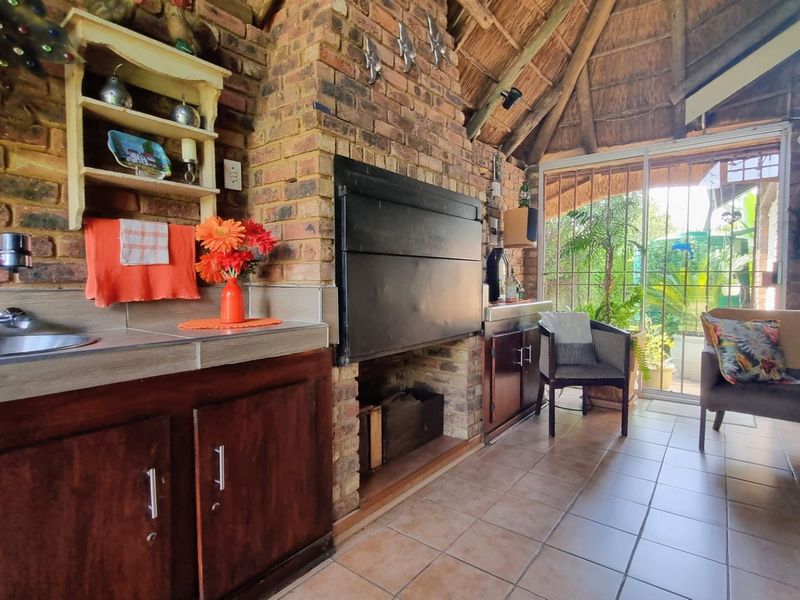 Covered patio area featuring a thatched roof, exposed brick walls, built-in braai, and a functional kitchenette with sink and cabinetry.