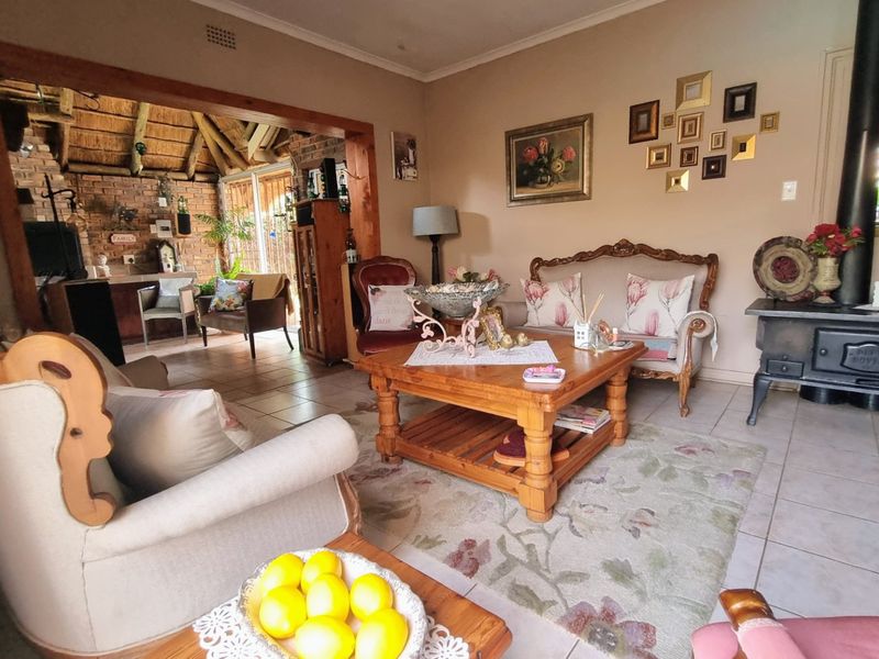 A cozy living room featuring tiled floors and a cast iron fireplace, opening into a rustic area with exposed brickwork and a thatched roof.