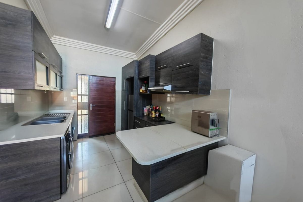 Modern kitchen featuring dark wood-grain cabinetry, stone countertops, a double sink, and tiled flooring with direct access to an exterior door.