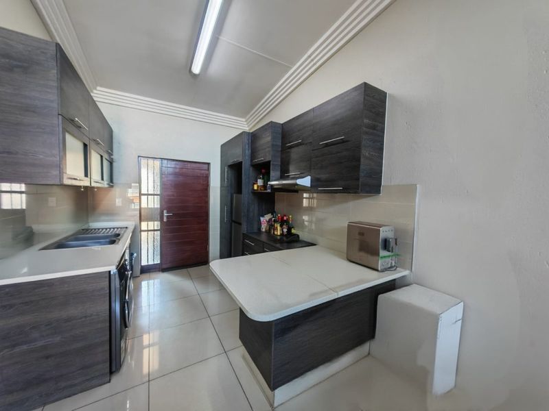 Modern kitchen featuring dark wood-grain cabinetry, stone countertops, a double sink, and tiled flooring with direct access to an exterior door.