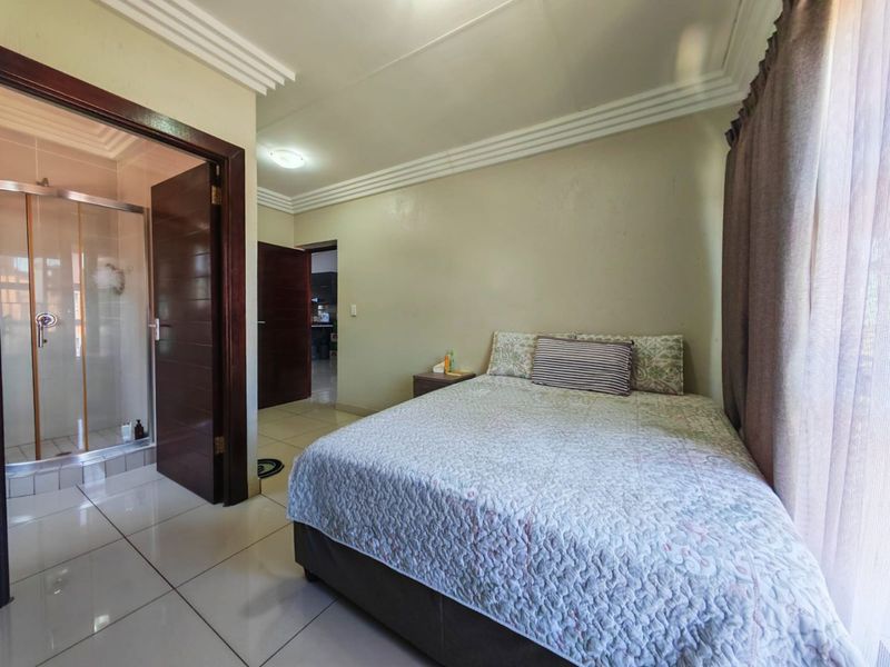 A bedroom featuring tiled flooring, crown molding, and an attached en-suite bathroom with a glass shower enclosure.