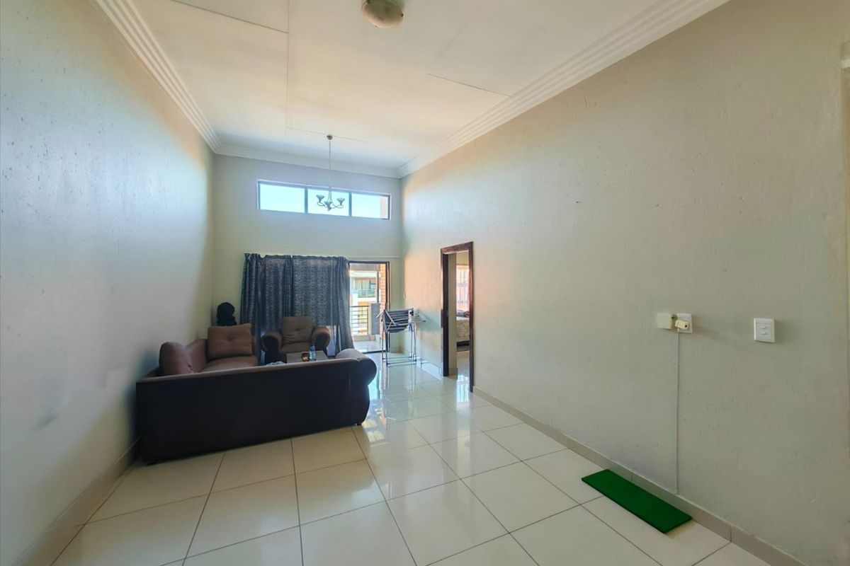 Spacious living area featuring high ceilings, large format floor tiles, and natural light through a transom window and sliding door access to the balcony.