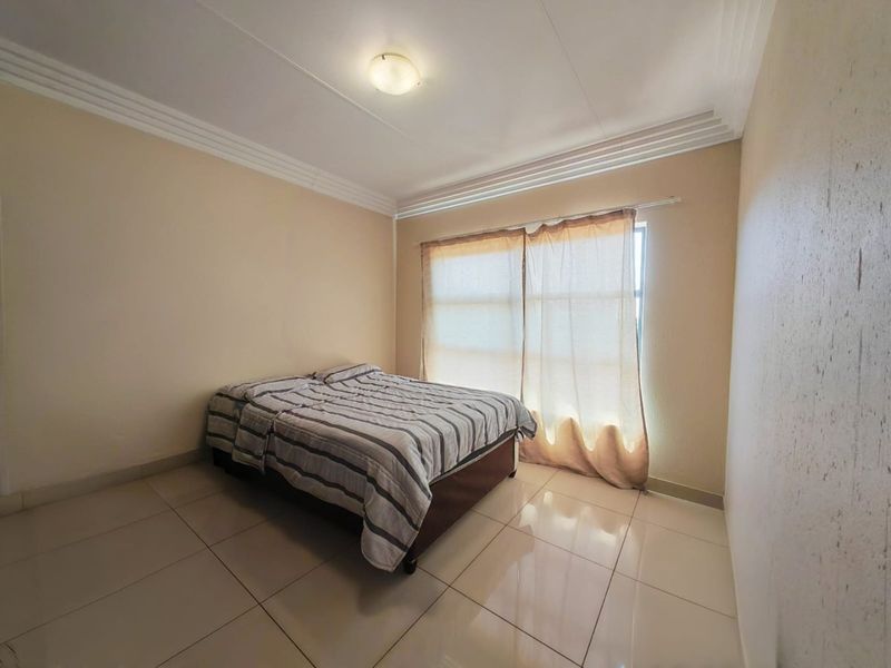 A simple bedroom featuring neutral wall tones, tiled flooring, and decorative ceiling cornicing, providing a clean and functional living space.