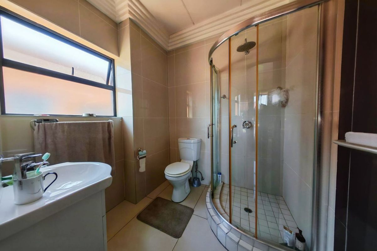 A functional bathroom featuring a corner shower enclosure, ceramic wall and floor tiles, a vanity basin, and a toilet.
