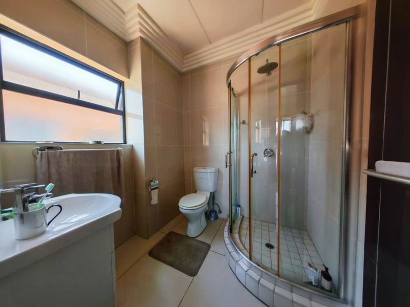 A functional bathroom featuring a corner shower enclosure, ceramic wall and floor tiles, a vanity basin, and a toilet.