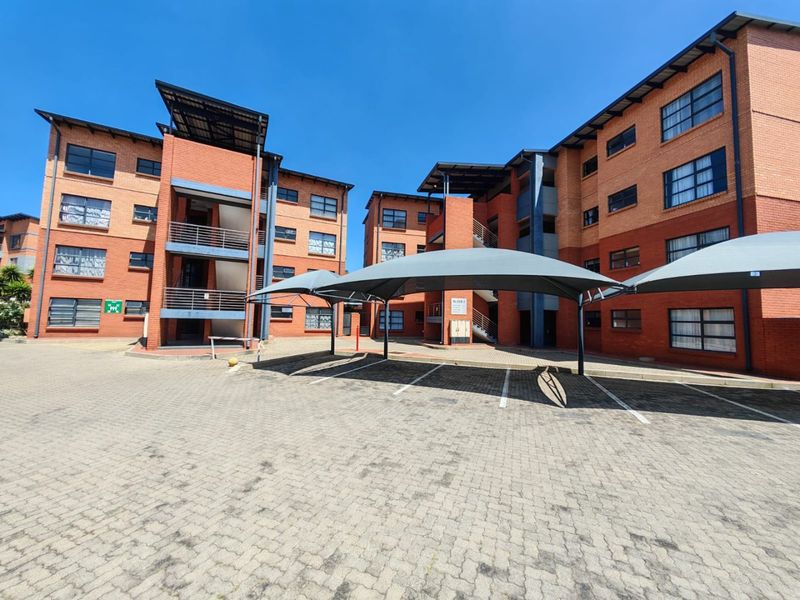 Exterior view of a multi-story apartment complex featuring red brick facades, paved parking area, and covered shade cloth carports.