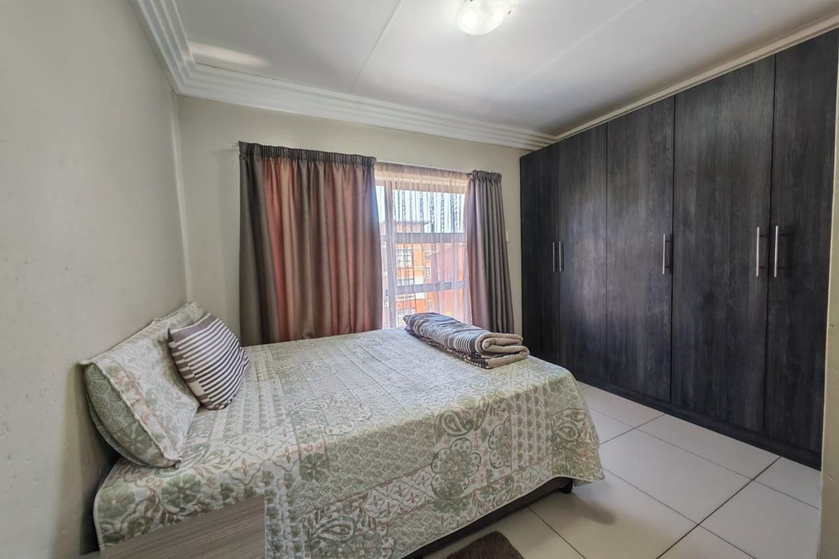 A well-maintained bedroom featuring large dark wood built-in cupboards, neutral tiled flooring, and classic ceiling cornice detailing.
