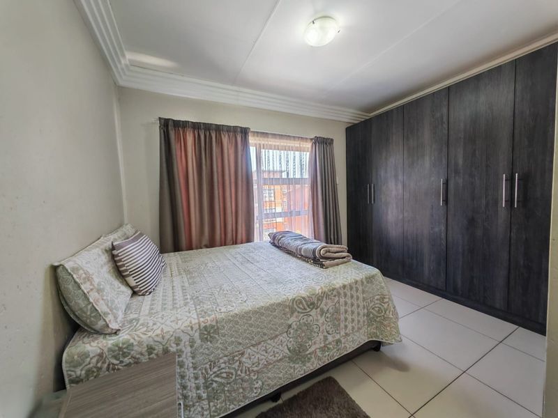 A well-maintained bedroom featuring large dark wood built-in cupboards, neutral tiled flooring, and classic ceiling cornice detailing.
