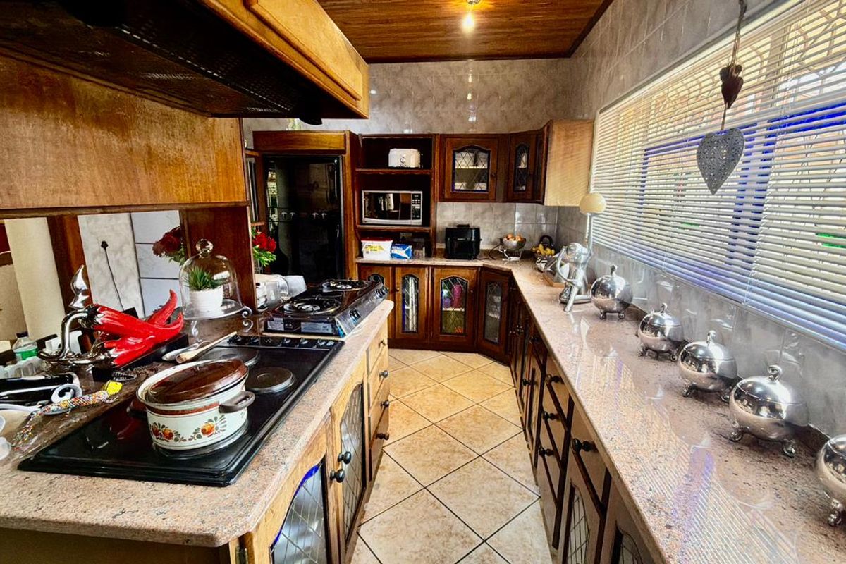 A traditional kitchen featuring extensive timber cabinetry, granite countertops, built-in hob with extractor, and tiled flooring.