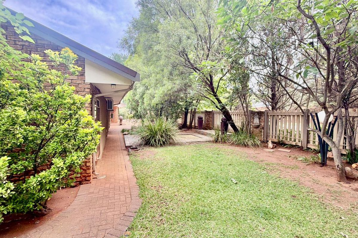 A view of the rear garden featuring a brick exterior wall, a paved walkway, and established trees and lawn.