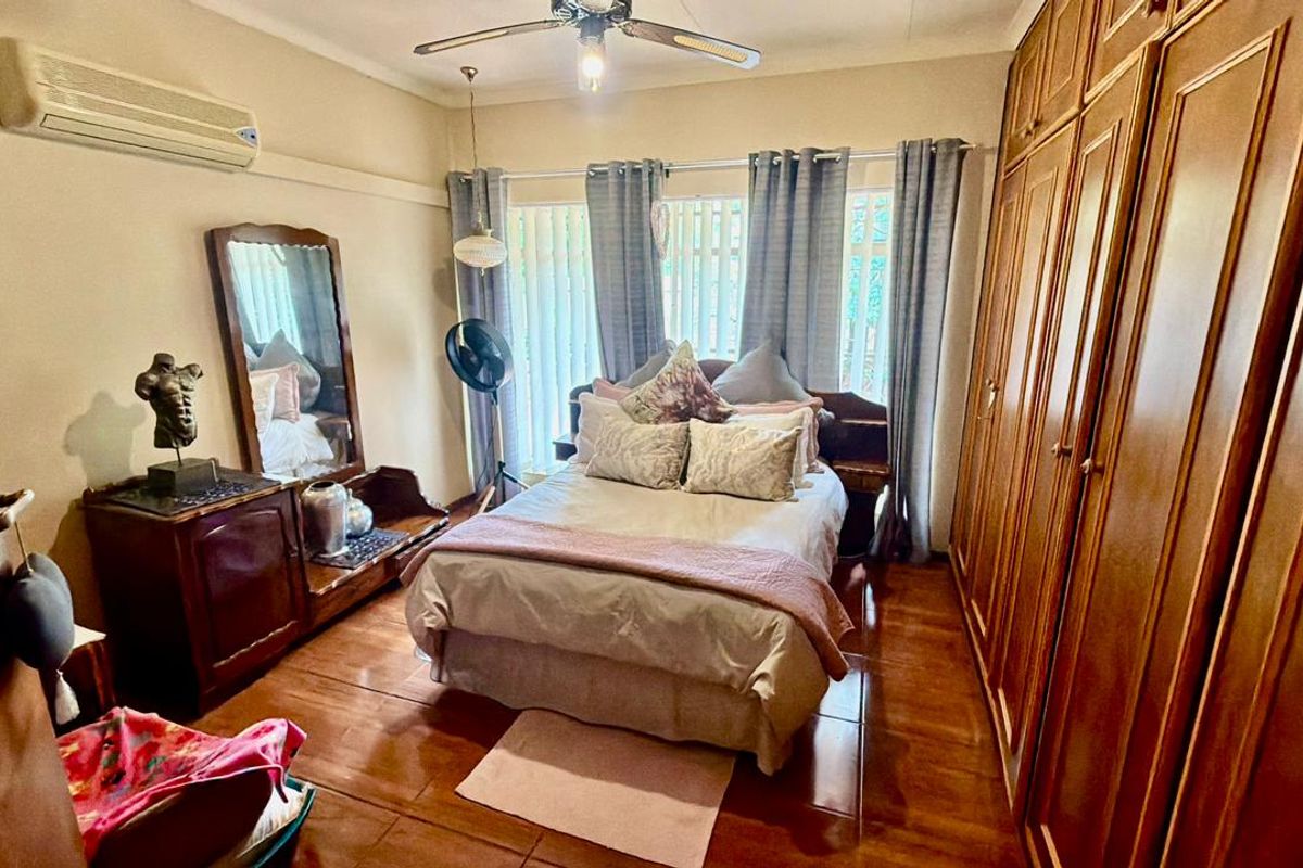 A bedroom featuring built-in wooden cupboards, tiled flooring, a ceiling fan, and a wall-mounted air conditioning unit.