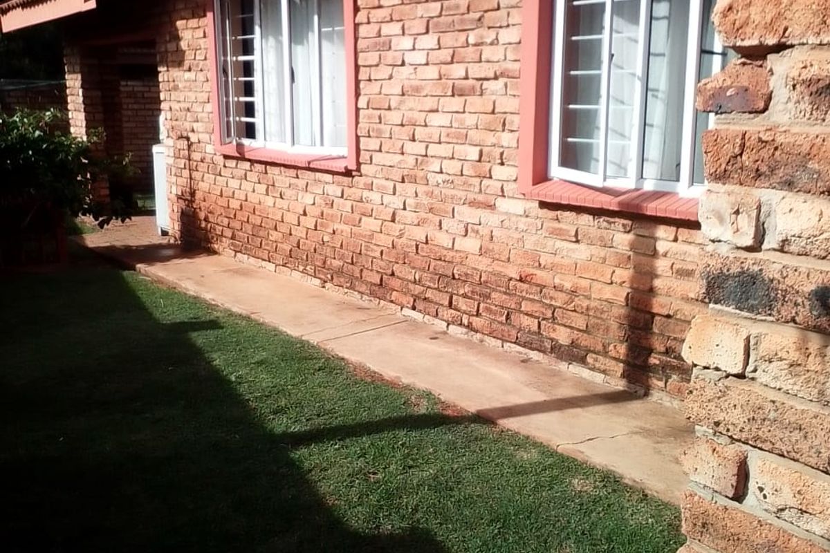 A view of the rear exterior of the townhouse featuring exposed brickwork, a tiled roof, and a concrete pathway alongside a small lawn.