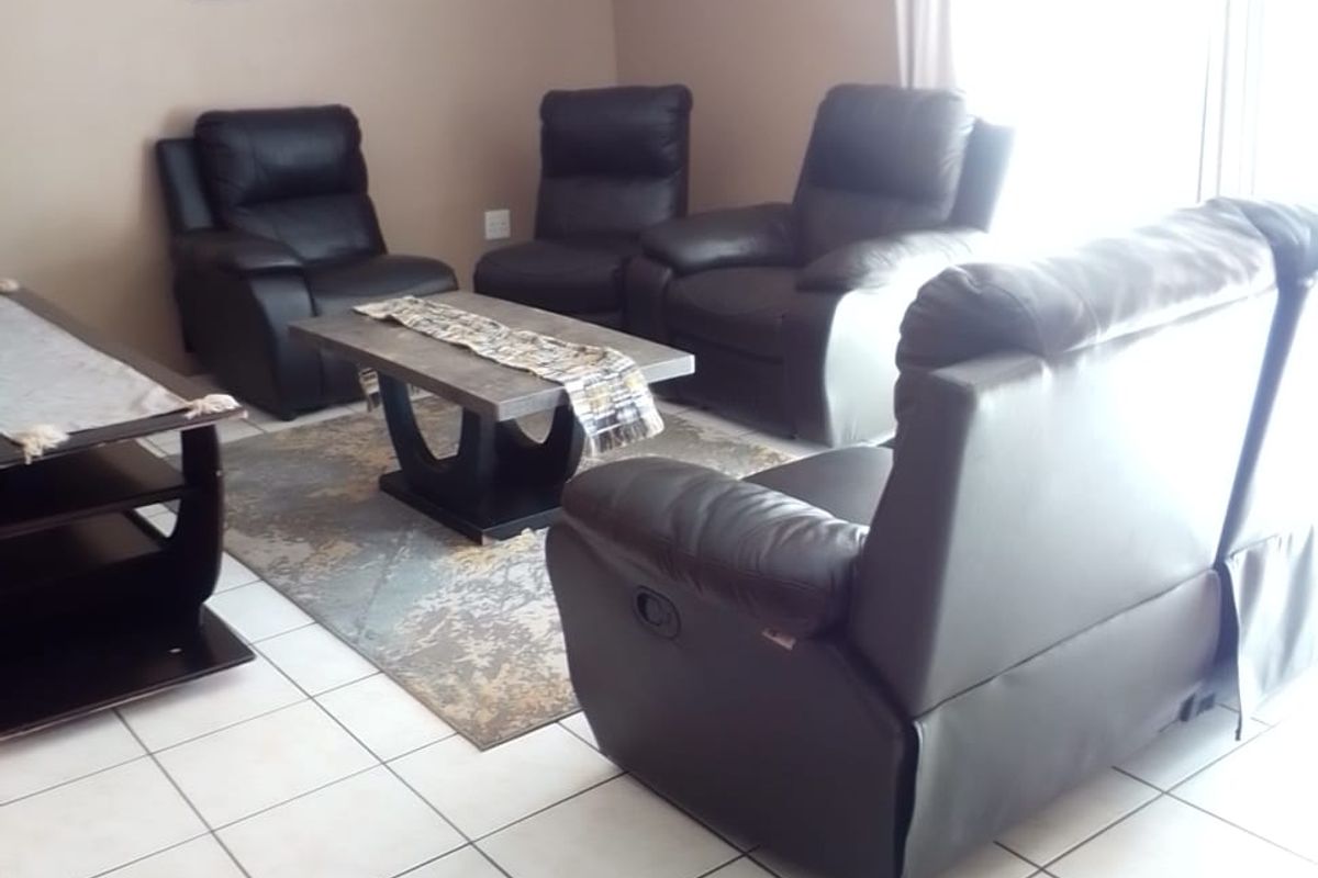 A living room area featuring neutral wall paint and light-colored ceramic floor tiles, with access to an outdoor area via a sliding glass door.