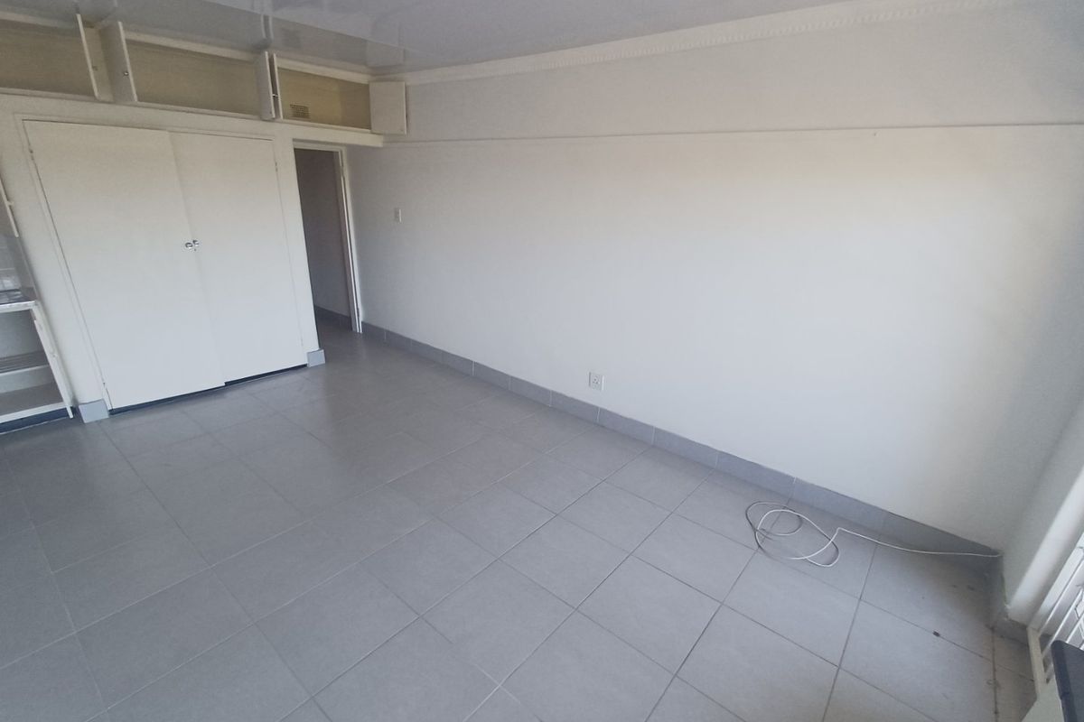 An empty, neutral-toned room featuring tiled flooring, built-in storage cupboards, and overhead storage compartments, offering a blank canvas for personalization.