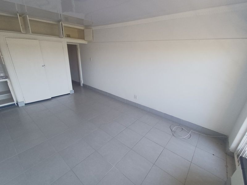 An empty, neutral-toned room featuring tiled flooring, built-in storage cupboards, and overhead storage compartments, offering a blank canvas for personalization.