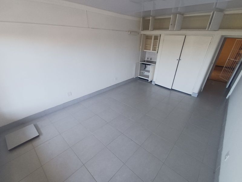 An empty studio apartment space featuring tiled flooring, built-in storage cupboards, and a small integrated kitchenette area.