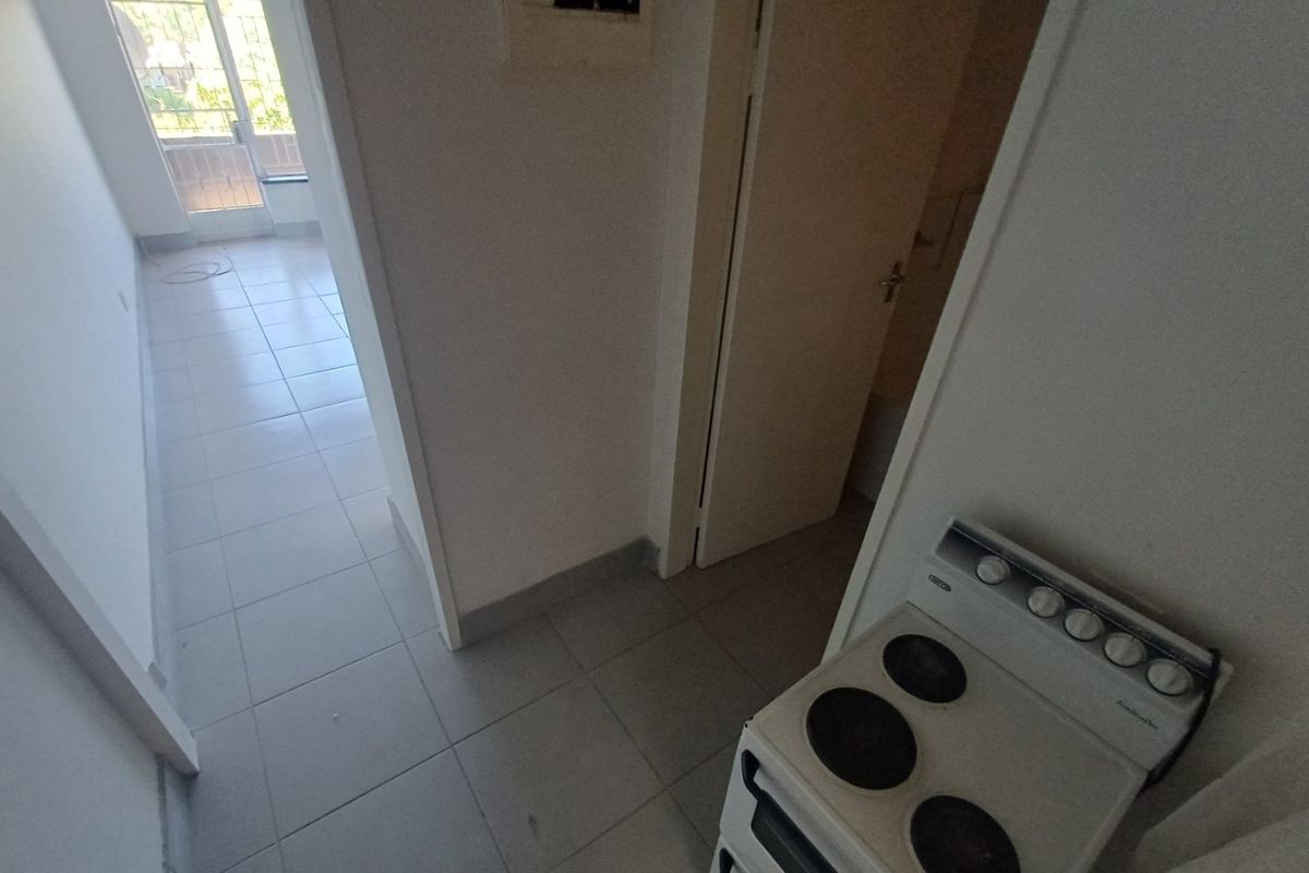 A view of a kitchen area featuring a freestanding stove, tiled flooring, and access to an adjacent room with a balcony.