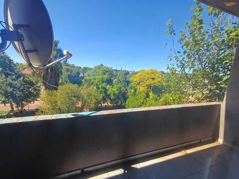 A balcony with tiled flooring and a solid wall ledge, offering an elevated view of the surrounding trees and neighborhood.