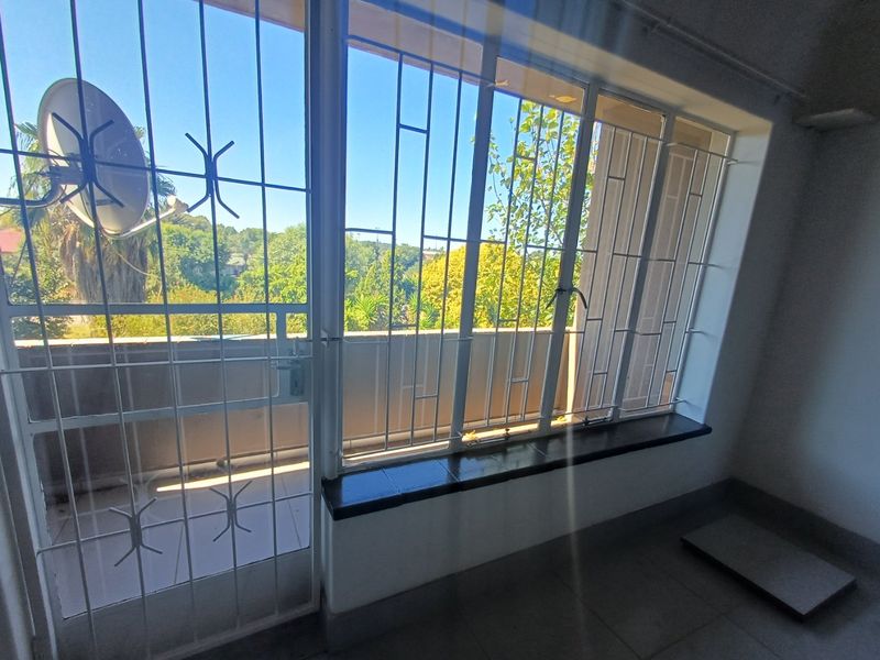 Interior view of a living area featuring large windows with security bars and direct access to an outdoor balcony space.
