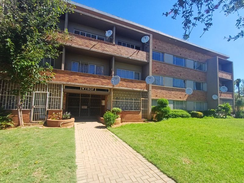 Exterior view of the Wynof apartment complex featuring a brick facade, paved walkway, and communal garden area.