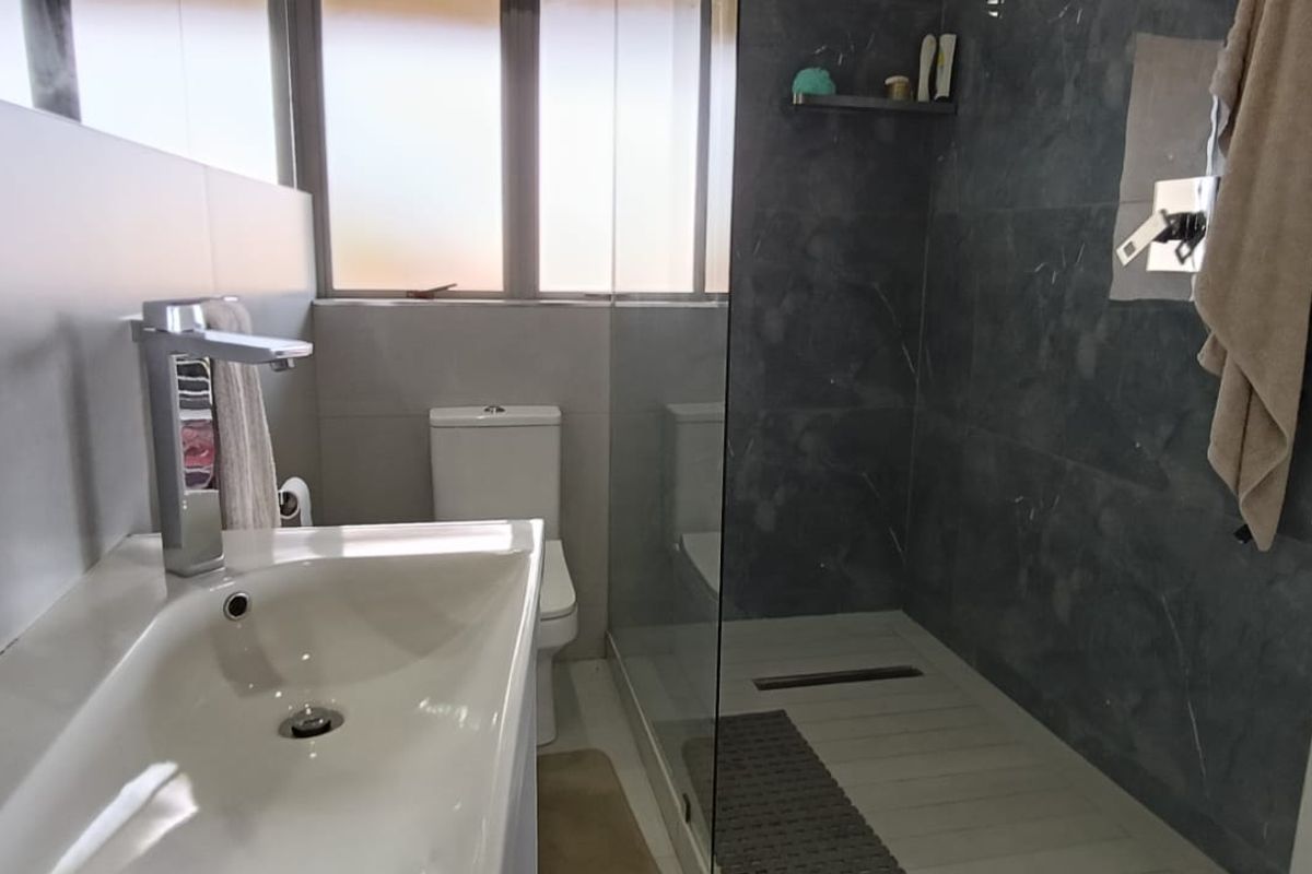 Modern bathroom featuring a walk-in shower with glass screen, contemporary basin with mixer tap, and neutral wall tiling.