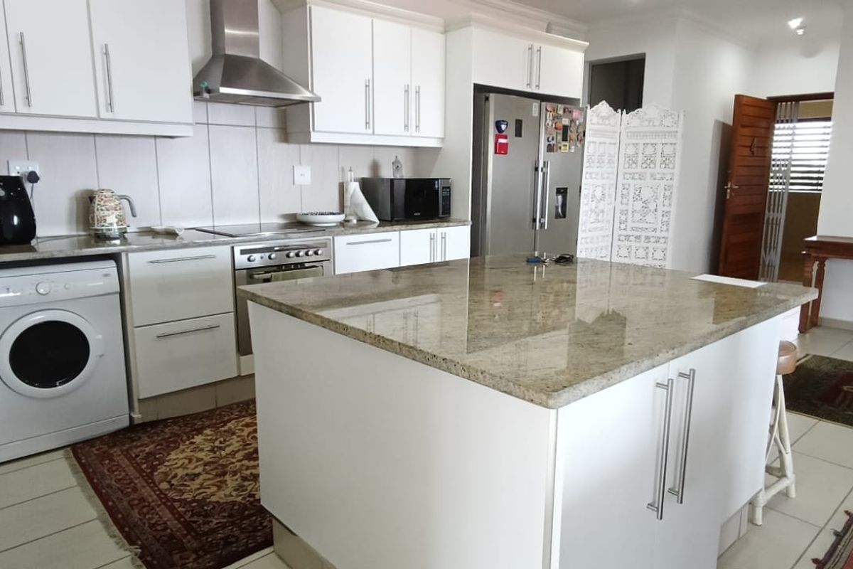 Modern kitchen featuring white cabinetry, granite countertops, a central island, and integrated stainless steel appliances, flowing into an open-plan living area.