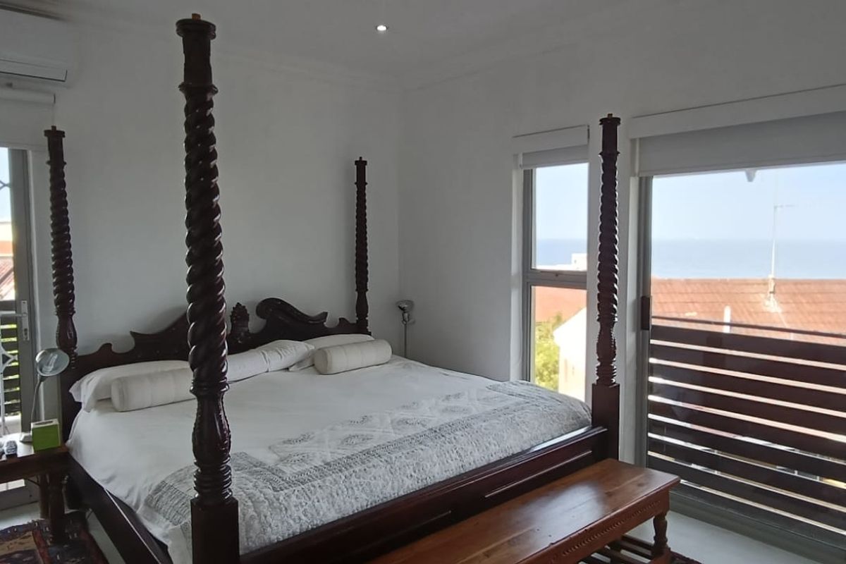 A bright bedroom featuring large sliding glass doors with access to a balcony, built-in air conditioning, and views of the surrounding area.