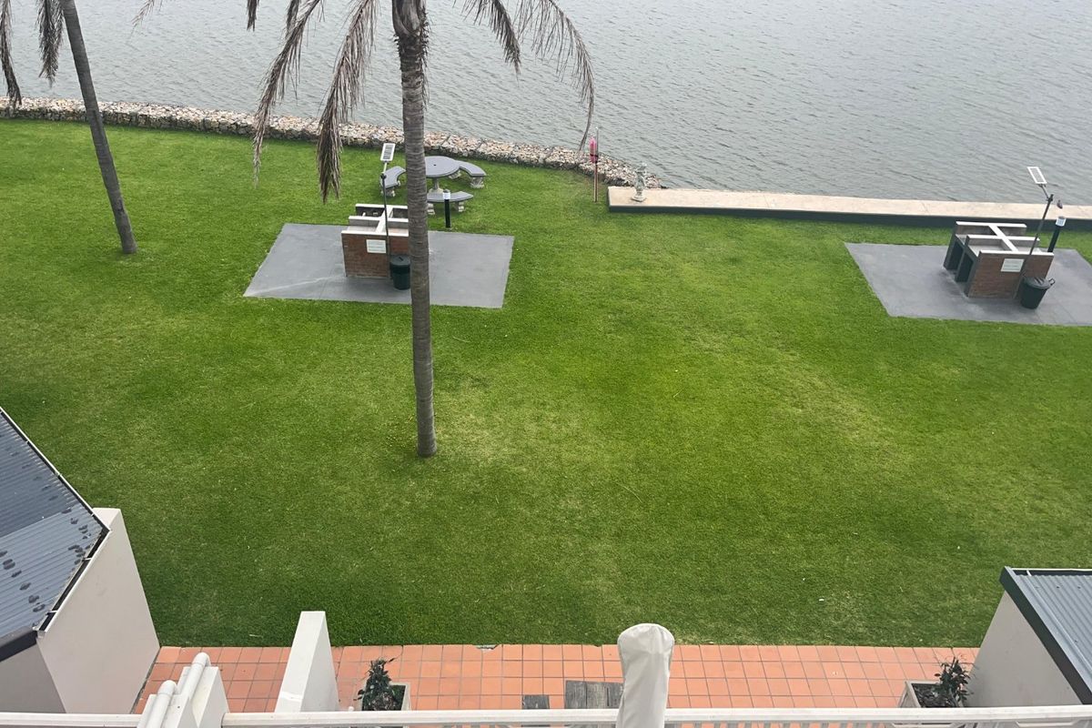 Elevated view of a communal rear garden featuring a lawn, built-in brick braai areas, and a waterfront retaining wall.