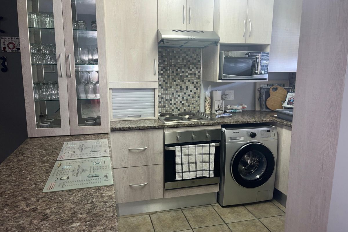 Compact kitchen featuring light wood-grain cabinetry, granite countertops, mosaic backsplash, and integrated appliances including an oven, hob, and washing machine.
