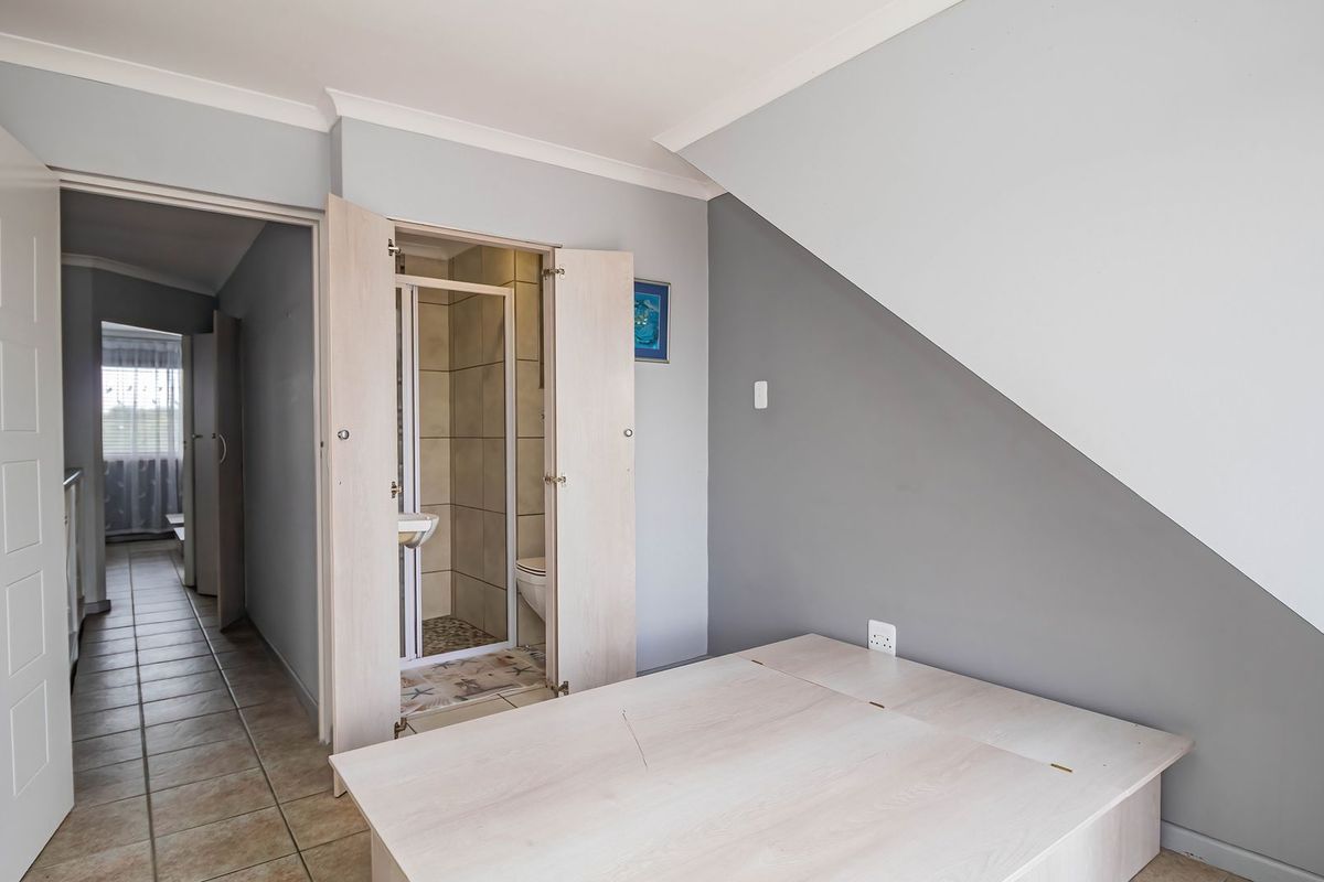 A bedroom featuring a sloped ceiling, tiled flooring, and an integrated en-suite bathroom with a shower.
