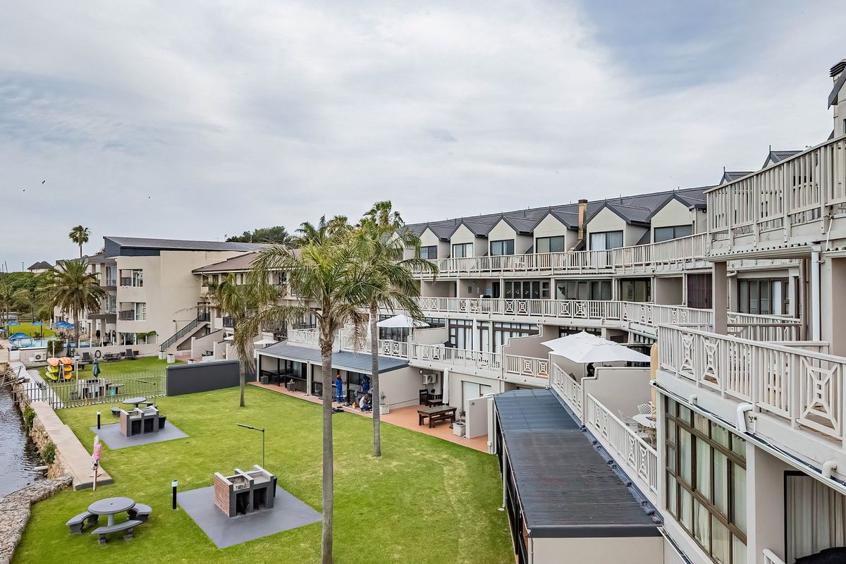 Elevated view of the apartment complex rear facade, featuring tiered balconies, communal lawn area with built-in braai facilities, and direct water frontage.