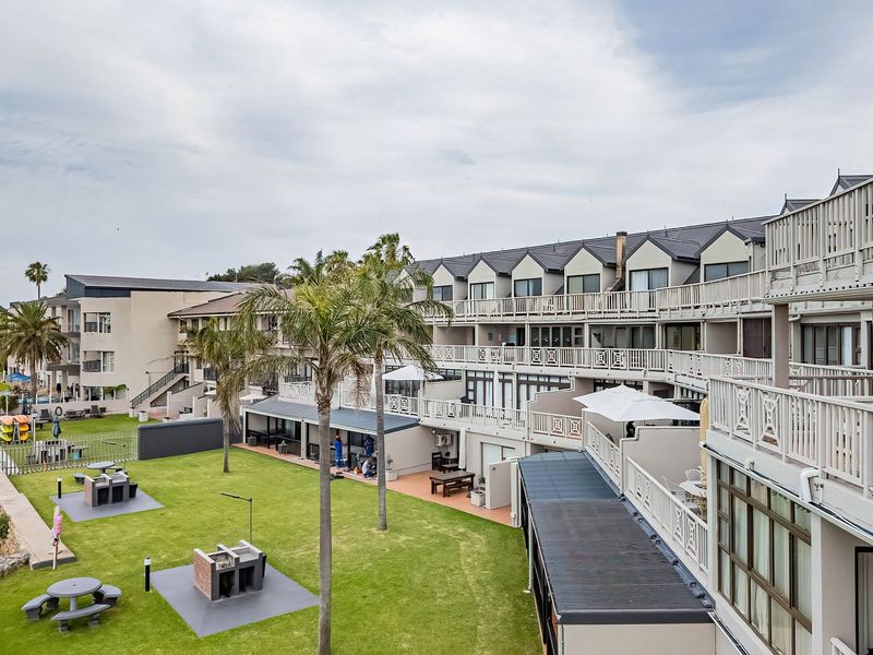 Elevated view of the apartment complex rear facade, featuring tiered balconies, communal lawn area with built-in braai facilities, and direct water frontage.