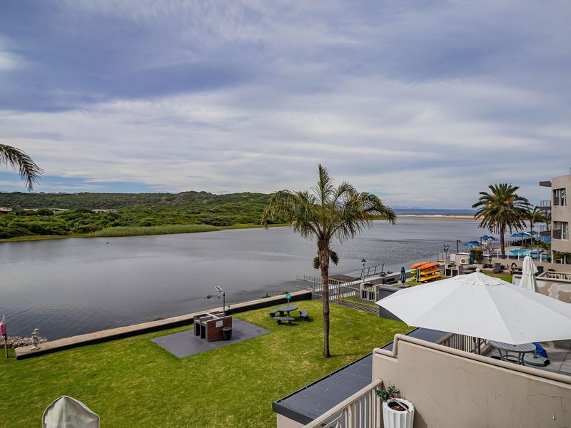 Scenic elevated view overlooking a river, landscaped garden, and communal outdoor area from a private balcony.