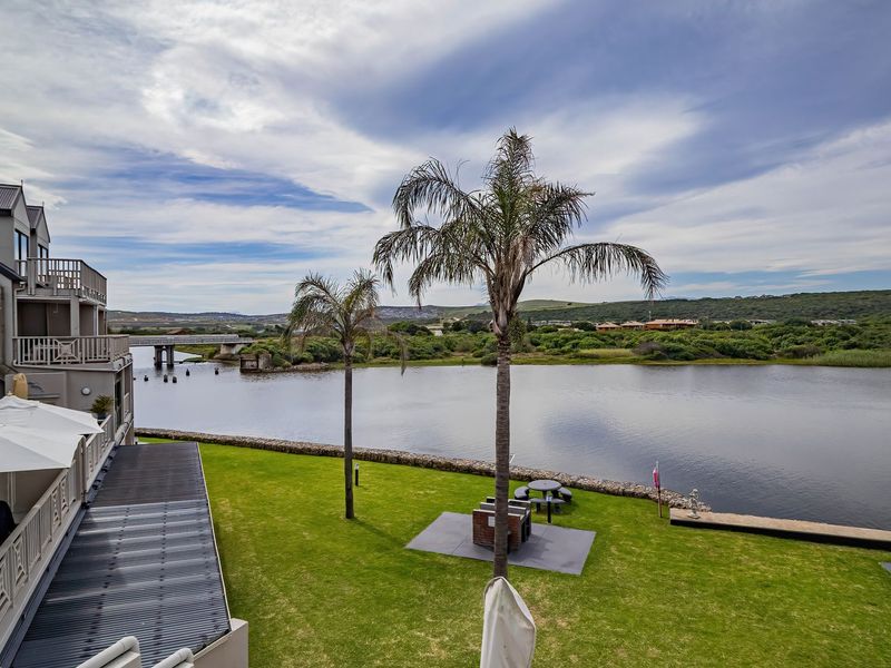 Scenic view overlooking a river and natural landscape, featuring a well-maintained lawn, built-in braai areas, and balcony access from the apartment building.