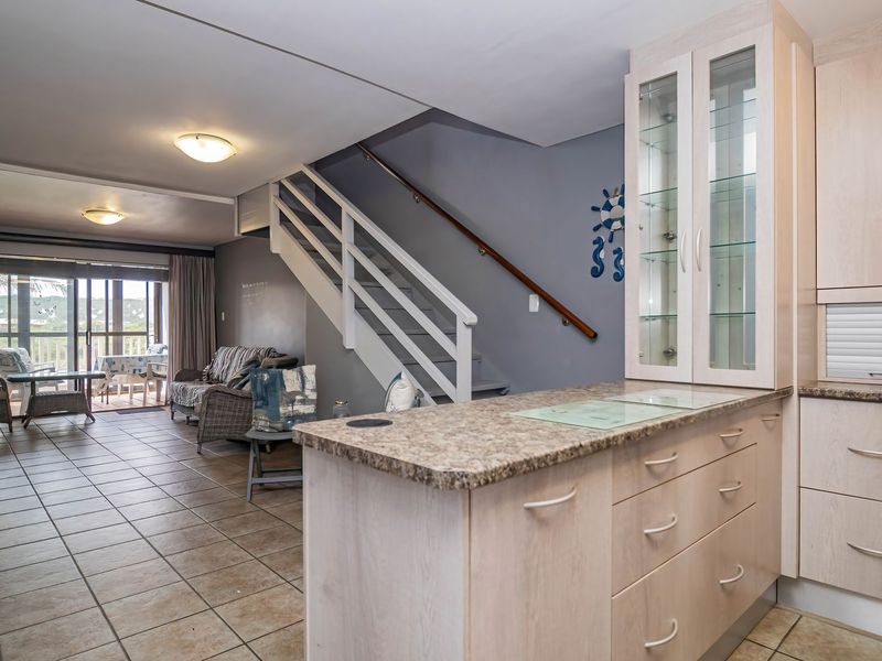 Open-plan living area featuring a functional kitchen with built-in cabinetry, tiled flooring, and a staircase leading to the upper level.