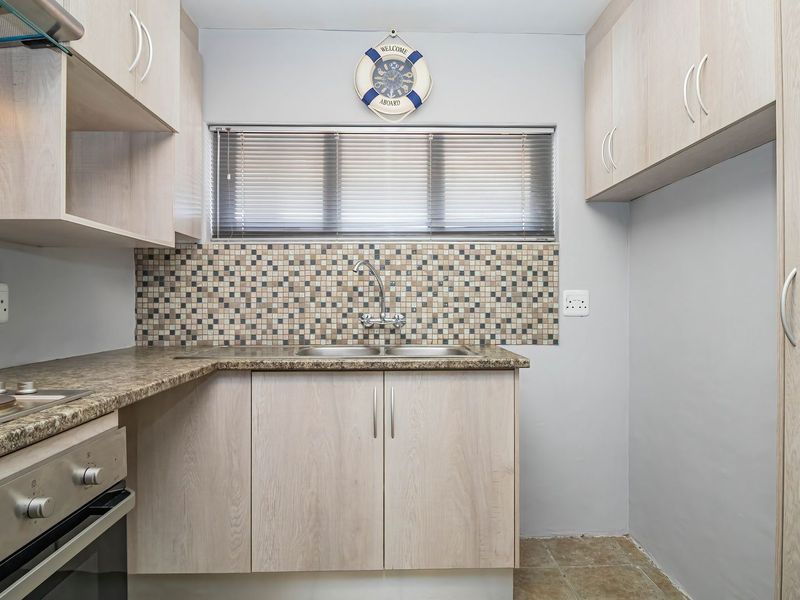 A functional kitchen featuring light wood-finish cabinetry, granite-look countertops, a mosaic tile backsplash, and integrated appliances including an oven and hob.