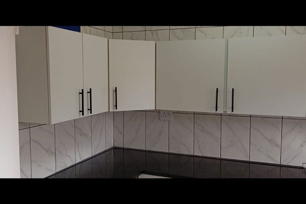 A clean, modern kitchen area featuring white cabinetry, black granite countertops, and marble-effect wall tiling.
