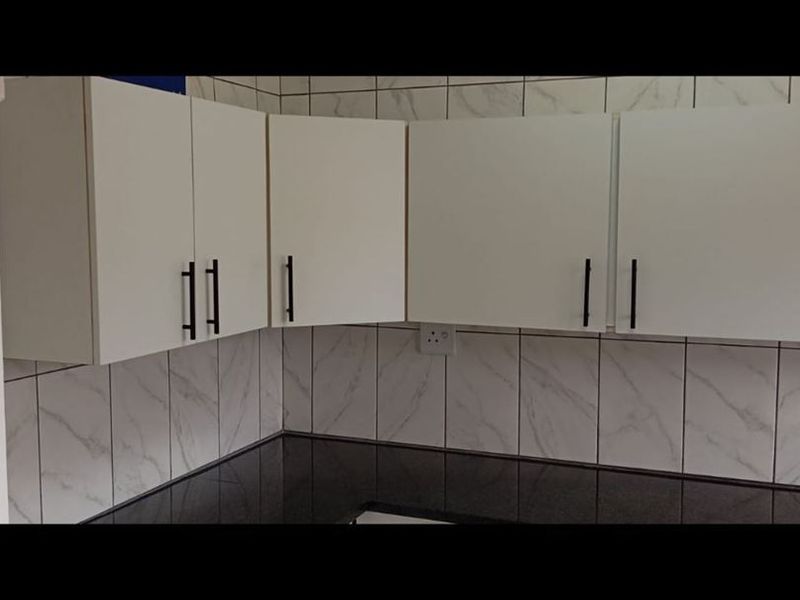 A clean, modern kitchen area featuring white cabinetry, black granite countertops, and marble-effect wall tiling.