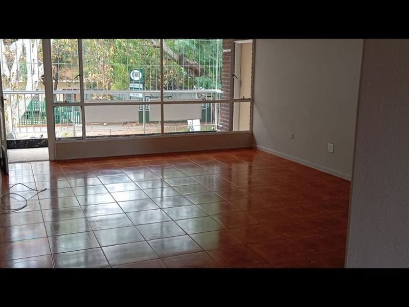 An empty, sunlit living area featuring polished tiled flooring and large windows with direct access to a balcony.