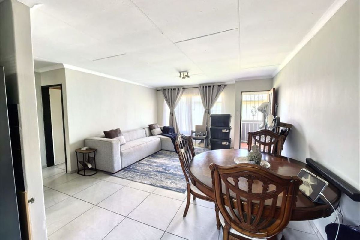 Open-plan living and dining area featuring tiled flooring, ceiling cornicing, and access to an outdoor balcony through a sliding glass door.