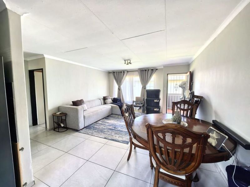 Open-plan living and dining area featuring tiled flooring, ceiling cornicing, and access to an outdoor balcony through a sliding glass door.