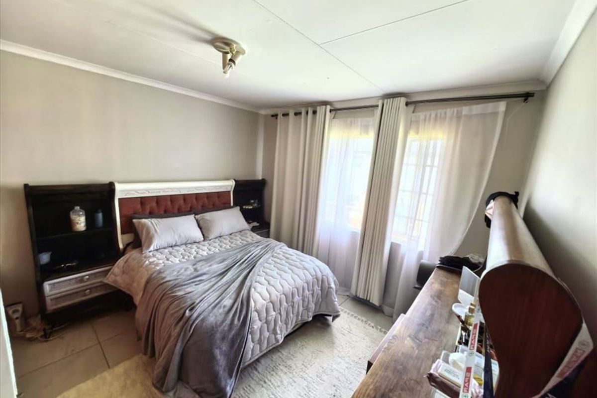 A functional bedroom featuring tiled flooring, neutral wall tones, and large windows with installed curtain tracks, providing a comfortable and well-lit living space.