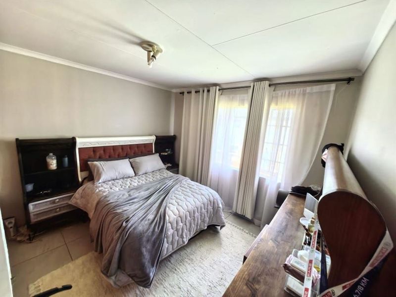 A functional bedroom featuring tiled flooring, neutral wall tones, and large windows with installed curtain tracks, providing a comfortable and well-lit living space.