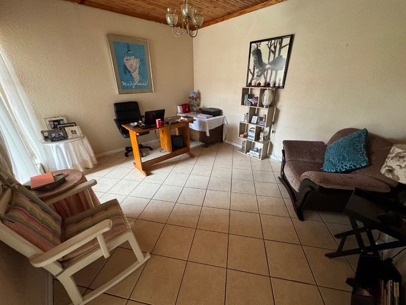 A living area featuring tiled flooring and a timber plank ceiling, currently utilized as a home office space.