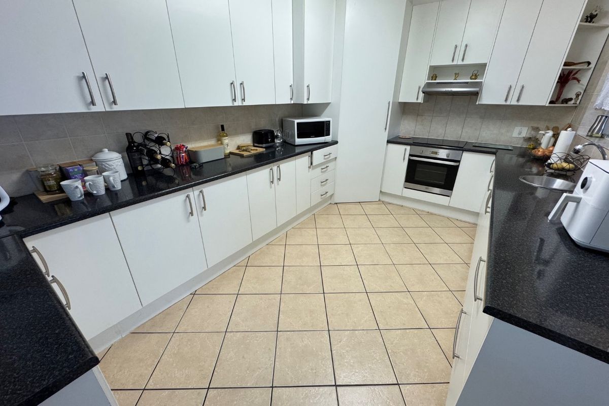 A functional kitchen featuring white cabinetry, dark granite countertops, built-in oven and hob, and tiled flooring with a neutral backsplash.