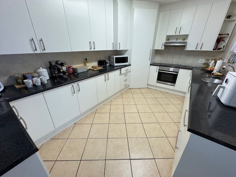 A functional kitchen featuring white cabinetry, dark granite countertops, built-in oven and hob, and tiled flooring with a neutral backsplash.
