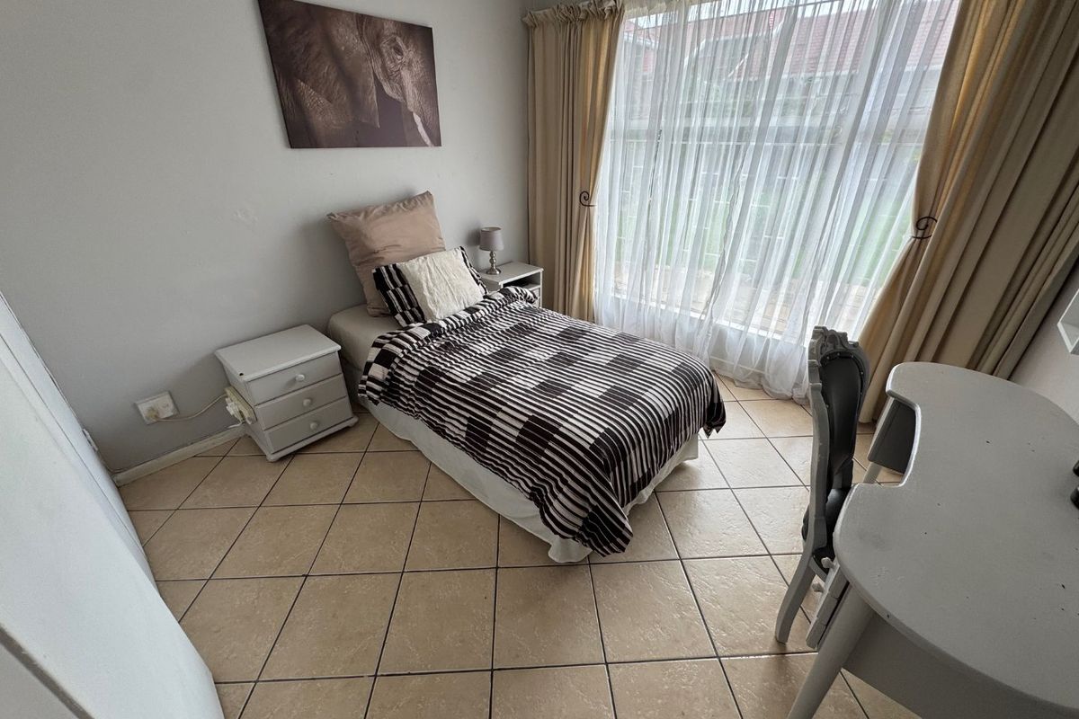 A functional bedroom featuring tiled flooring and a large window with curtain tracks, providing natural light and a view of the exterior.
