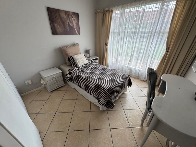A functional bedroom featuring tiled flooring and a large window with curtain tracks, providing natural light and a view of the exterior.