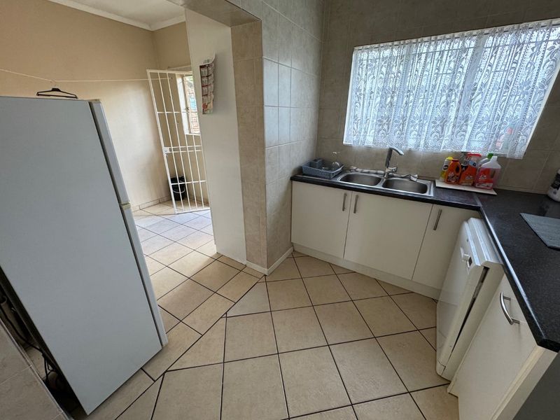 Functional kitchen featuring tiled flooring, built-in cabinetry, laminate countertops, and a double bowl stainless steel sink with a window view.