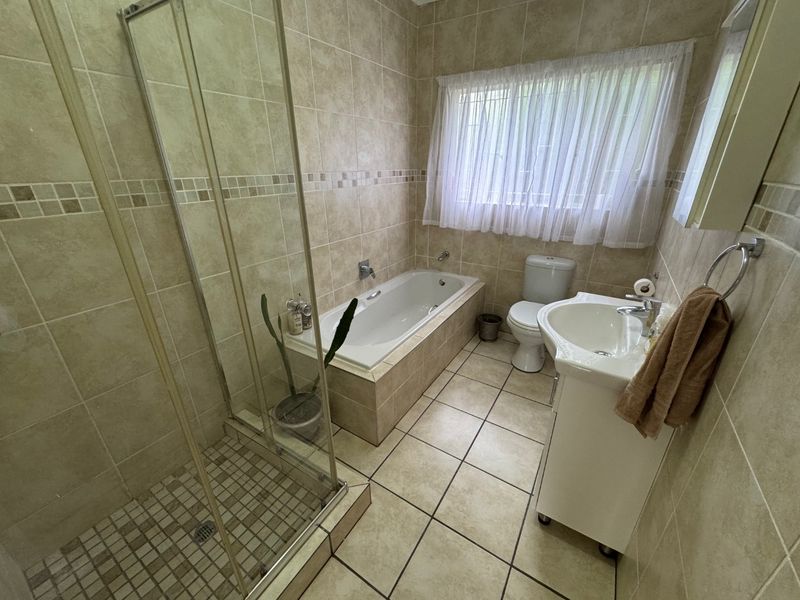 A functional bathroom featuring a glass shower enclosure, built-in bathtub, pedestal sink, and toilet with neutral ceramic tiling throughout.